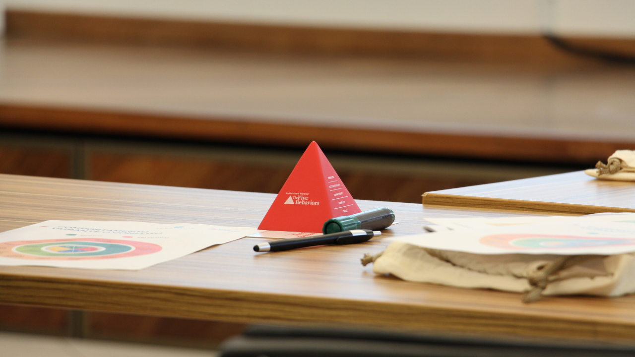 Fotografia de uma pirâmide vermelha pequena, em cima de uma mesa. Ao lado, vê-se papéis e canetas.
